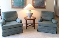 Photo showing the two blue fabric armchairs with patterned upholstery and a small round wooden table between them holding the ceramic lamp.