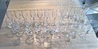 Top-down view of 30 assorted glass stemware pieces arranged in rows on a wooden table, showing variety in height and design.
