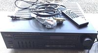 Front and top view of Teac AG-1000 stereo receiver with remote control and cables on top, placed on ground.