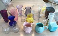 Glass vases and ceramic pitchers arranged on a table showing variety of colors, shapes, and materials.