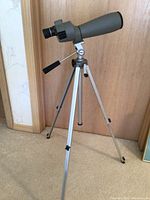Side view of Velbon telescope mounted on silver tripod with adjustable legs, showing eyepiece and handle for adjustment.