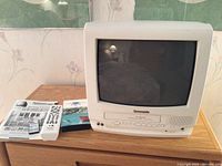 Panasonic vintage CRT TV with VHS player, remote controls, manuals, and fishing VHS tape on wooden desk.