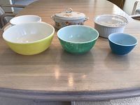 Front view of colorful Pyrex mixing bowls, covered casserole dishes, and Corelle items shown on table