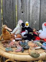 Photo shows a variety of Beanie Babies arranged on a wicker chair, including a duck, flamingo, bald eagle, red fox, crab and several smaller wolf plush toys.