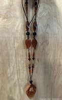 Full view of the necklace showing the hand carved leaf beads and various other beads on braided string.