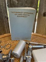 Close-up photo of a light blue book titled 'Fair Market Appraisal of Used Dental Equipment' and some visible metal dental props.
