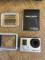 Close-up of GoPro HERO3+ camera, Battery BacPac manual, and clear protective housings including Battery BacPac cover