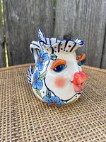 Side view of the fish-shaped ceramic creamer showing painted blue flowers, orange lips and eyelashes, and detailing on the fin.
