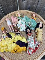 Top view of 8 vintage dolls in various conditions, some missing limbs, arranged in a woven basket.