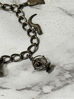 Close-up of ship's wheel charm and part of chain links on marble surface.