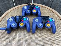 Four indigo blue wired Nintendo GameCube controllers on a wicker table.