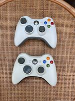 Top view of two white Xbox 360 controllers showing buttons and analog sticks.