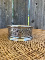 Front view of small silver dish showing floral engraved details on metal surface and slight tarnish.