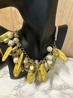 Front view of vintage statement necklace on black bust showing yellow howlite stones with round white and translucent beads on chain and braided cord.