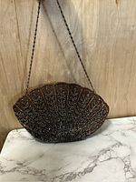Front view of brown vintage beaded purse shaped like a scallop fan with detailed beadwork and chain strap against wood and marble background.