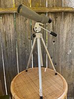 Side view of vintage Bushnell spotting scope mounted on adjustable tripod with pan handle mount.