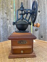 Front and side view of vintage coffee grinder showing wooden base with drawer labeled 'CAFE' and cast iron grinder with hand crank and wooden handle knob.