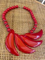 Front view of the vintage red Bakelite necklace showing the full design with round beads and curved leaf-shaped pendants on a woven surface.