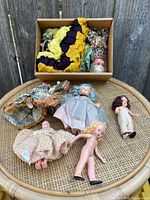 Top view of vintage dolls laid out on wicker chair including some dolls with crocheted dresses and blue and blonde hair dolls