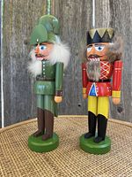 Front view of two nutcracker soldier figurines, one in green uniform with fur, the other in red and yellow with crown and fur.