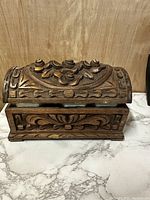 Front view of the vintage wooden trinket box showing detailed floral carvings on the lid and geometric on the side panels.