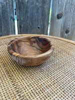 Side view of a small wooden bowl sitting on a woven surface showing its curved shape and wood grain detail.