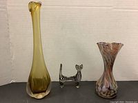 Wide shot showing all three items: tall amber bud vase, glass cat figurine, small multicolor vase.