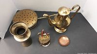 Photo showing five brass and copper items including tea pot, vase, warming pan, musical carousel horse, and a small copper plate