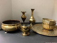 View of all brass items: 12-inch round tray, large footed bowl, two vases, small pitcher and stacked small bowls