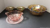 Wide shot showing all carnival glass pieces including large bowl, two candlestick holders, two smaller bowls, cranberry bowl and matching plate.