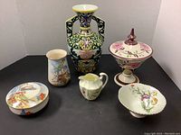 All six ceramic items arranged together showing vase, covered bowl, creamer, scalloped bowl, cylindrical vase, and lidded bowl.