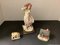 Photo showing the ceramic girl figurine with geese and two small ceramic cottages arranged on a flat surface.