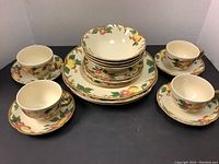 Full set of Johnson Bros Peachland dinnerware showing arrangement of 4 dinner plates, 4 side plates, 4 bowls, 4 cups and 4 saucers with matching peach, leaf and flower design and gold trim.