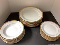 Set of stacked dinner plates, side plates, and bowls showing gold patterned rims