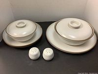 Photo of two covered casserole dishes each sitting on round platters, plus salt and pepper shakers in front