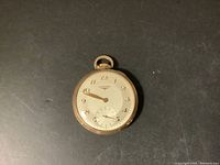Front view of pocket watch showing white dial, gold-tone numerals, hands, and small seconds register