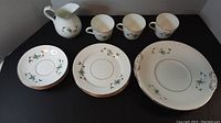 Full set view of 3 cups, 3 saucers, 2 side plates, and 1 pitcher arranged on a black surface