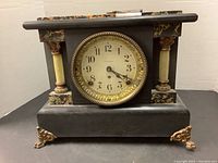 Full front view of the vintage Seth Thomas mantel clock showing black body with marble-patterned sections, ornamental beige columns with gold decoration, and ornate gold legs.