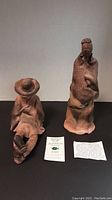 Two red clay pottery figures shown on a black surface with two small cards of description in front.