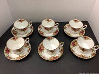 Complete set of 6 cups and saucers arranged on black surface showing floral and gold trim design.