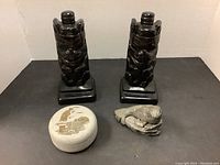 View showing set of two black soapstone bookends, carved seal sculpture, frog sculpture, and circular soapstone bowl with lid.