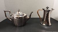 Front view of silver plate tea pot and milk jug showing shapes, handles and finish.