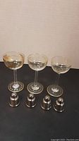 Three vintage sherry glasses with gold designs on the bowls and bases alongside four small silver salt and pepper shakers.
