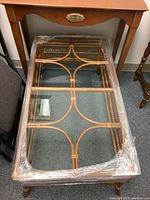 Top view of the glass tabletop showing the wicker frame underneath and plastic wrap on the edges.