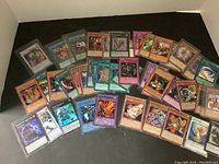 Image showing a spread of about 40 Yu-Gi-Oh! trading cards with a mix of monster, spell, and trap cards in various colors; many cards are in protective sleeves.