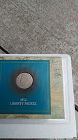 Photo showing the 1912 Liberty Nickel housed in a protective display holder with blue background and the year 1912 labeled below the coin.