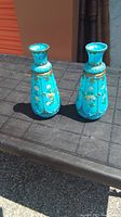 Photo of two blue glass vases with hand painted floral designs and gold accents, placed side by side