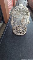 Full view of the cast metal birdcage showing overall shape, size, and design details including the dome top and base.