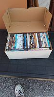 Photo of an open cardboard box filled with many DVD movie cases stacked vertically inside.