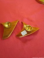 Pair of vintage wooden mid century modern candle holders on a red fabric background. Each has a brass cup to hold a candle.